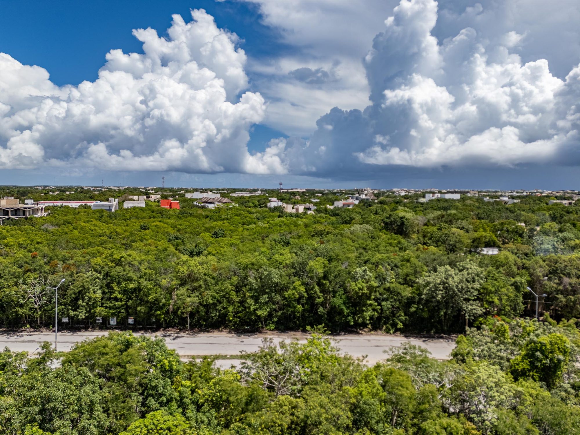 Aerial view over the 5th Avenue lots in downtown Tulum, dense jungle canopy under tall cumulus clouds